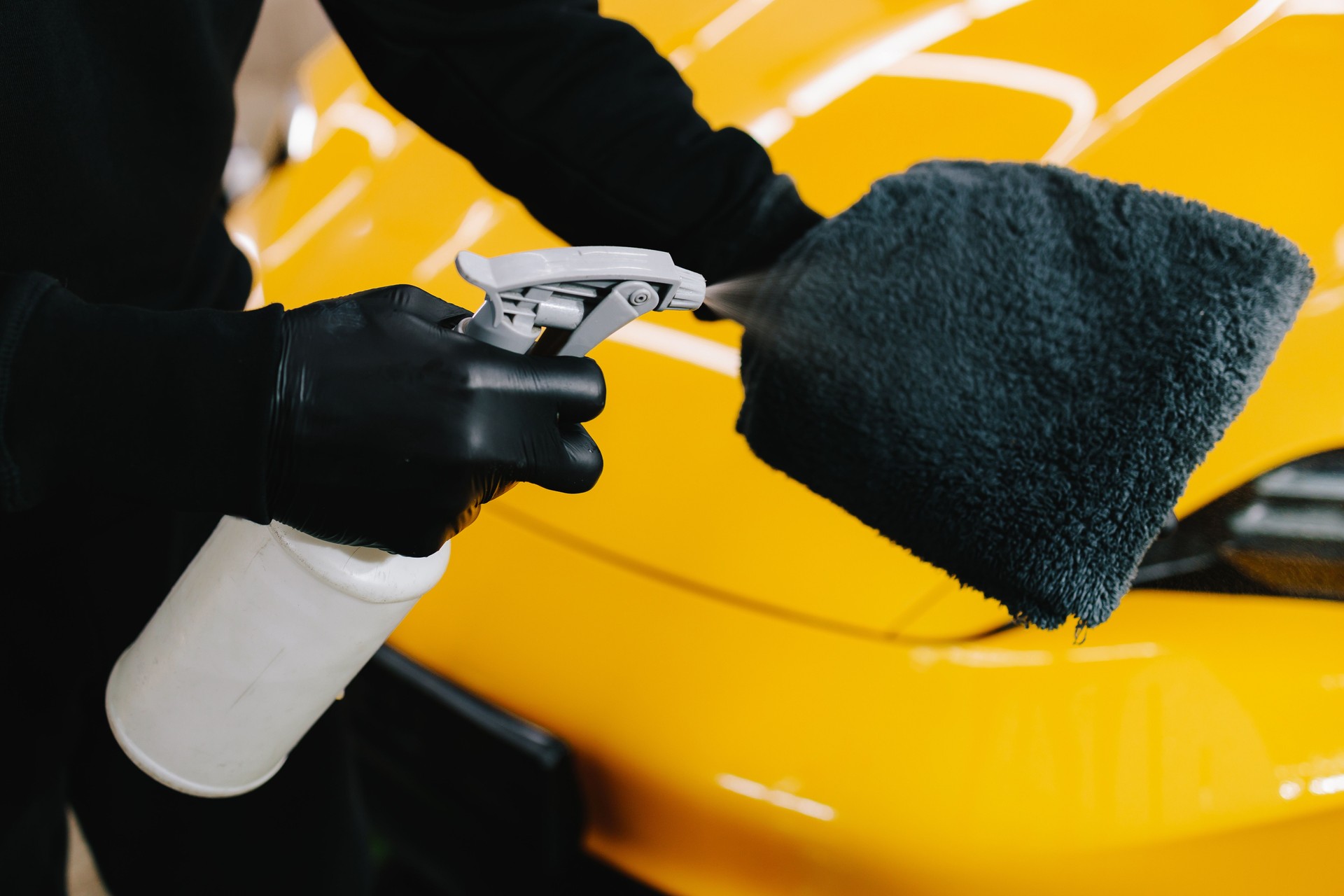 Car cleaner spraying liquid for waxing on microfiber cloth at the service. Detailing process with using spray wax product for car protection.